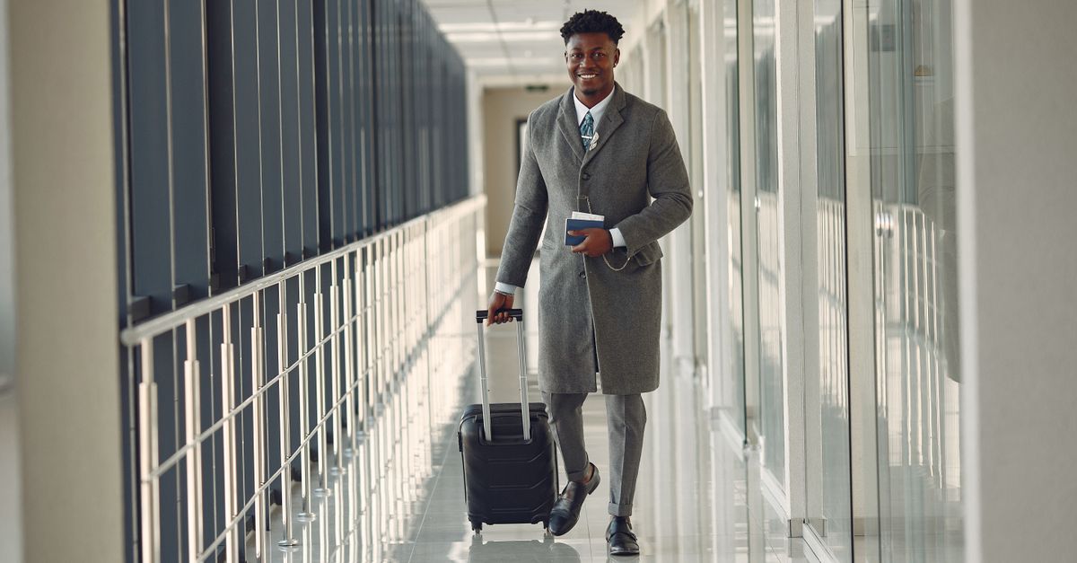 Homme d'affaires en transit dans un aéroport avec valise cabine et carte d'embarquement