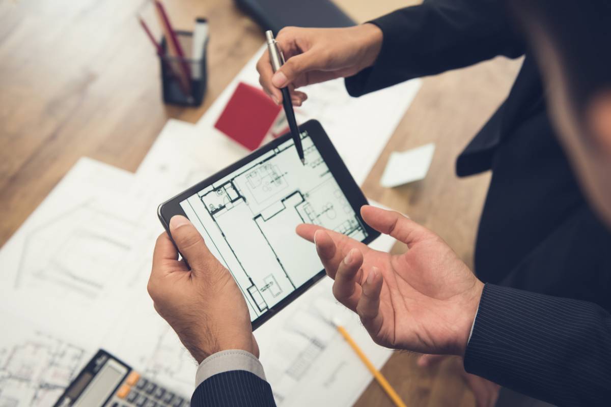 Plan 2D d'un logement consulté sur une tablette au-dessus de plans papier