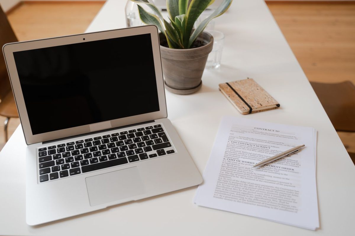 Ordinateur portable, contrat et carnet de notes posés sur un bureau clair
